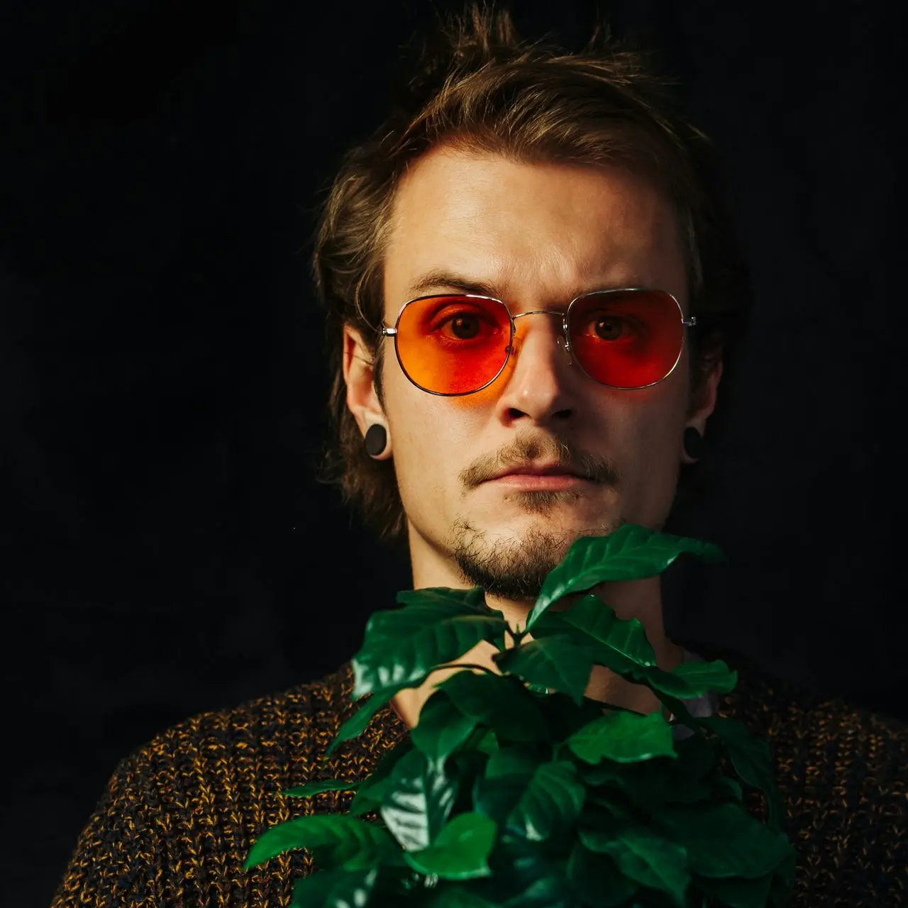 man in black and white long sleeve shirt wearing sunglasses standing beside green plant